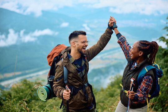 Cheerful couple of hikers holding hands while celebrating their climbing to top of mountain.
