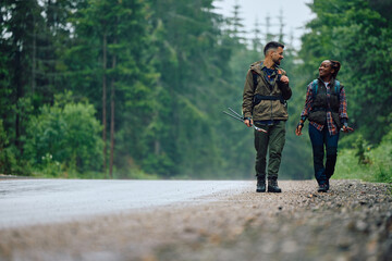 Multiracial couple walks by road while hiking in woods.
