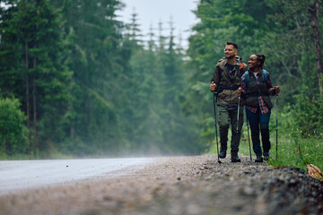Young happy couple of hikers walk by road in nature.