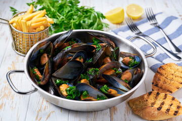 Mussels with french fries and herbs in cooking pan. White background. Close up.