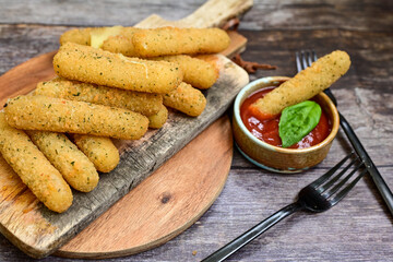 Vegetarian italian cheese breaded  oven baked  mozzarella sticks with  fresh basil on wooden background Italain street food