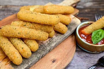 Vegetarian iitalian cheese breaded  oven baked  mozzarella sticks with  fresh basil on wooden background.Italian street food.