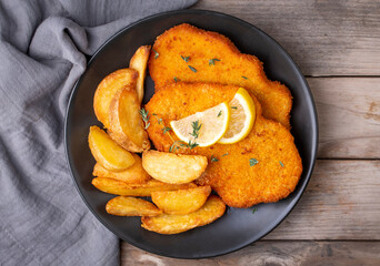 Chicken schnitzel with sauce, fried potatoes and lemon in a plate