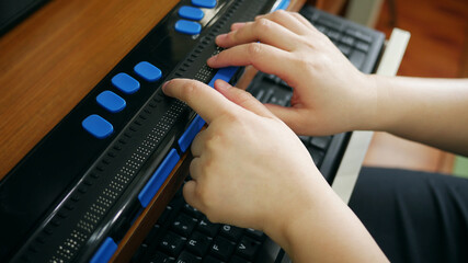 Close-up hands of person with blindness disability using computer with braille display or braille...