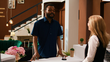 Tourist registering at front desk with hotel concierge, talking to hotel staff about leisure activities at exotic summer resort. African american guest arriving in lobby, preparing to check in.