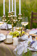 Elegant fancy wedding table decor with bright ranunculi flowers in a vase outdoors, chandelier, field or meadow. Summer, sunset, golden hour. Romantic dinner for a couple in restaurant outside