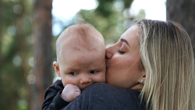 Cute little newborn rested his head on mom's shoulder. Loving mom kisses her adorable son on the ear. Blurred backdrop.