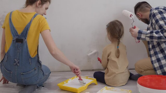Happy couple and little daughter painting wall and having fun during house renovation. Redesign and improvement new home for family. slow motion