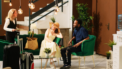 Hotel staff talking to guests in lobby, offering luxury services to people waiting in lounge area. Employee recommending tropical leisure activities to couple with room reservation.