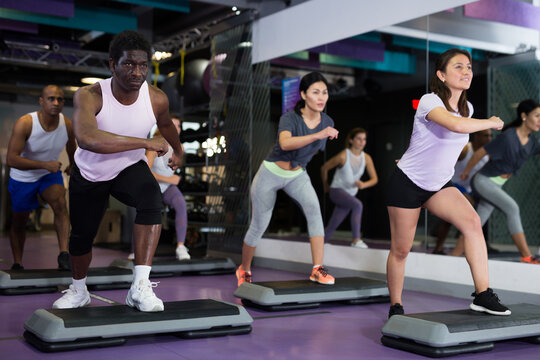 Sporty women and men doing cardio exercises training with step platforms at fitness center