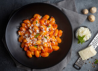 Traditional Italian food potato gnocchi with tomato sauce, parmesan cheese and fresh basil on dark table. Top view. Healthy food.