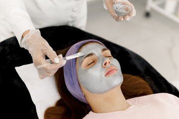 The cosmetologist applies a facial silver mask to the woman's face. Silver face mask. Cosmetology...
