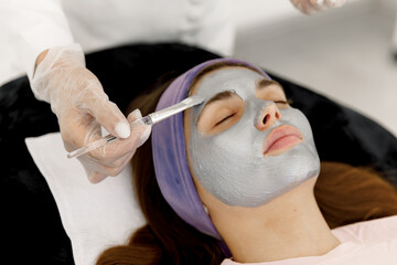 The cosmetologist applies a facial silver mask to the woman's face. Silver face mask. Cosmetology and facial skin care in beauty salon. 