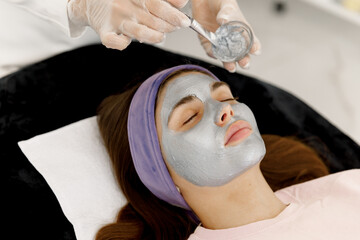 The cosmetologist applies a facial silver mask to the woman's face. Silver face mask. Cosmetology and facial skin care in beauty salon. 