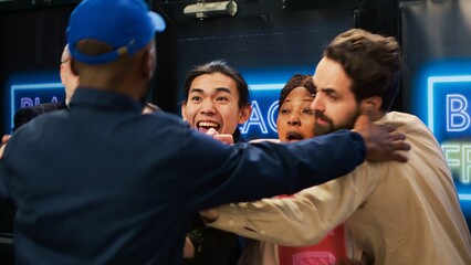 Anxious people wait in line for deals, standing in behind red tape at clothing store entrance. Mad crowd pushing barrier to open for black friday discounts, aggressive shoppers. Handheld shot.