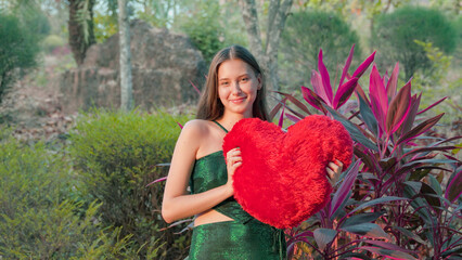 young woman with a large red heart on Valentine's Day against red flowers