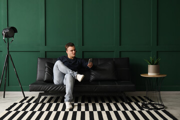 Young man using mobile phone on black couch in living room