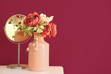 Vase with flowers and mirror on table near pink wall