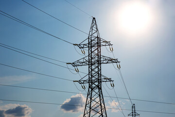 The concept of a source of electricity. Energy industry. High voltage tower with power wires against the background of the sun and clouds.