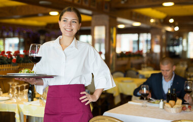 Fototapeta na wymiar Female waiter standing with serving tray, recommending dishes in restaurant