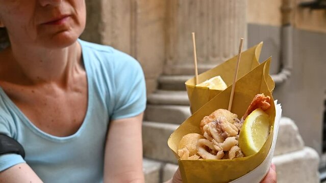 Genoa, Liguria, Italy. 3 june 2023. Slow motion footage of two takeaway fish fry cones: Genoa street food specialty. A middle-aged woman holds them up.