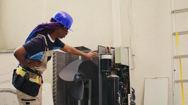 Precise mechanic commissioned for external hvac system routine maintenance, looking for damaged electric components. Skilled african american electrician doing condenser safety check
