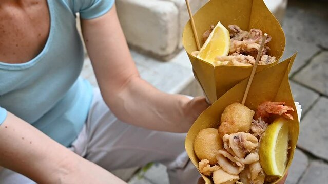 Genoa, Liguria, Italy. 3 june 2023. Slow motion footage of two takeaway fish fry cones: Genoa street food specialty. A middle-aged woman holds them up.