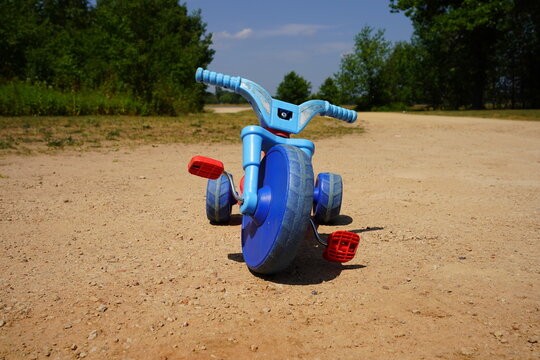 Blue and red used toddler tricycle big wheel bike sitting outside.