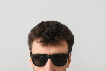 Young brunette man in sunglasses on light background, closeup