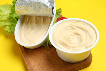 Wooden board with box of processed cheese and vegetables on yellow background
