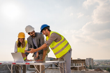 Diverse team of specialists with computer on construction site. Building project with engineers