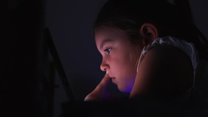 Child girl watching cartoons or social media or game on the tablet at night. Eyes are too close to the screen. Bad habit, insomnia problem