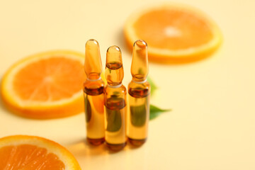 Ampoules with vitamin C and orange slices on beige background
