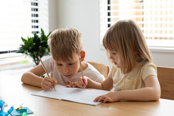 Brother and sister write and draw together with pencils at the table. The concept of home schooling