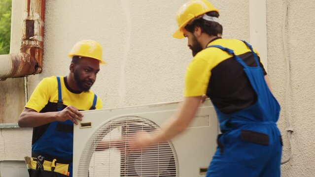 Teamworking diverse specialists starting work on damaged hvac system, taking apart condenser coil panel. Skilled wiremen dismantling air conditioner to check for bad wiring