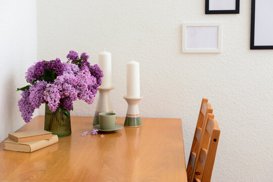 Vase with beautiful lilac flowers, candles on table and blank pictures in interior of light living room, closeup