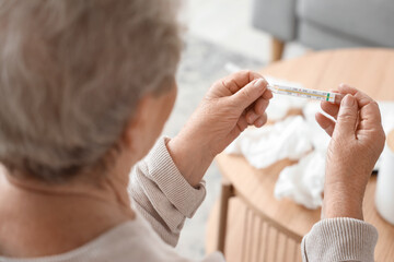 Ill senior woman with thermometer at home, closeup