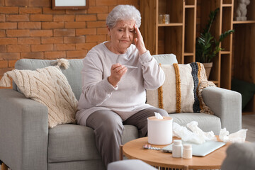 Ill senior woman with thermometer at home