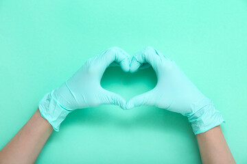 Female hands in medical gloves making heart gesture on turquoise background