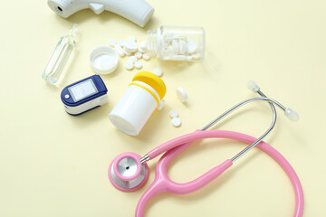 Stethoscope, pills, pulse oximeter and ampule on yellow background