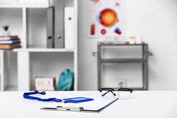 Clipboard, badge and eyeglasses on table in doctor office