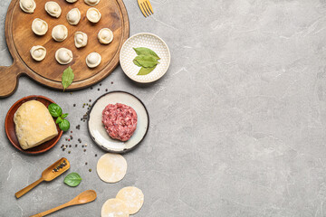Fototapeta na wymiar Wooden board with uncooked dumplings and ingredients on grey background