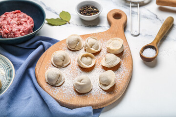 Wooden board with uncooked dumplings on white marble background