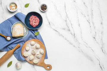 Wooden board with uncooked dumplings and ingredients on white marble background
