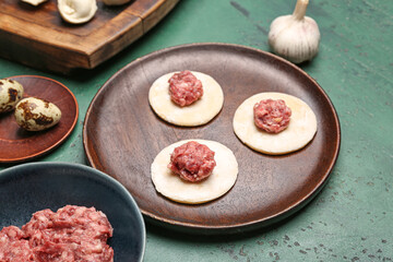 Plate of raw dough with minced meat for preparing dumplings on green background