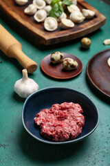 Bowl with minced meat for preparing dumplings on green background