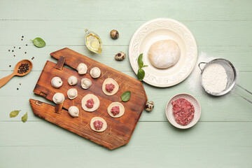 Board with uncooked dumplings and ingredients on green wooden background