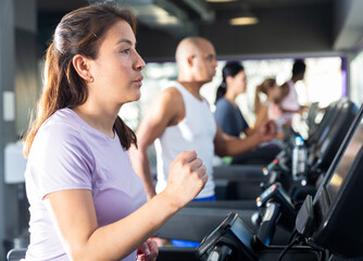 Fototapeta na wymiar Positive girl running on treadmill in fitness club