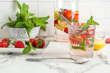 Glass and jug of fresh lemonade with strawberry on white table