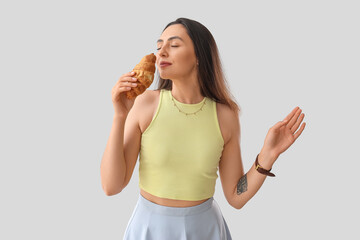 Young woman with tasty croissant on light background